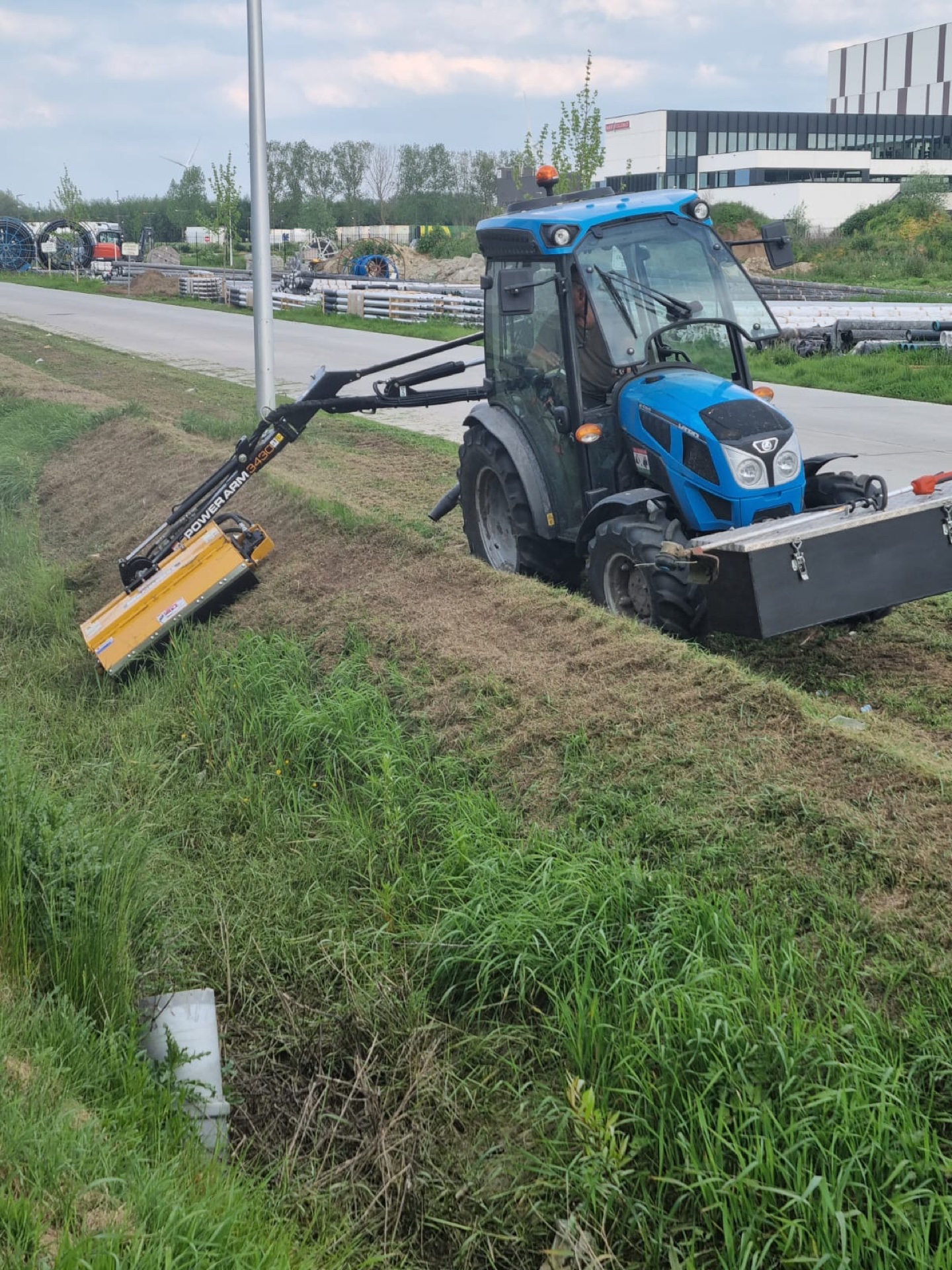 Tractor met maaiarm in actie op een berm